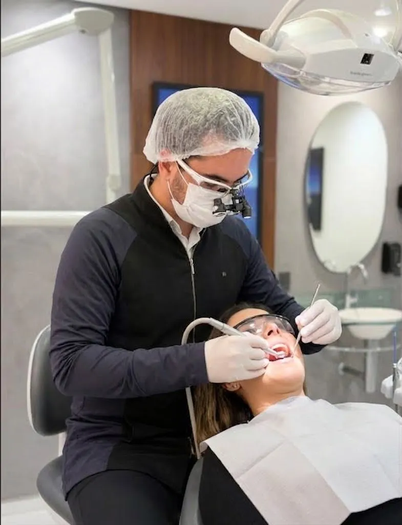 Dr. Victor Lopes atendendo uma paciente na cadeira odontológica, com lupa de aumento